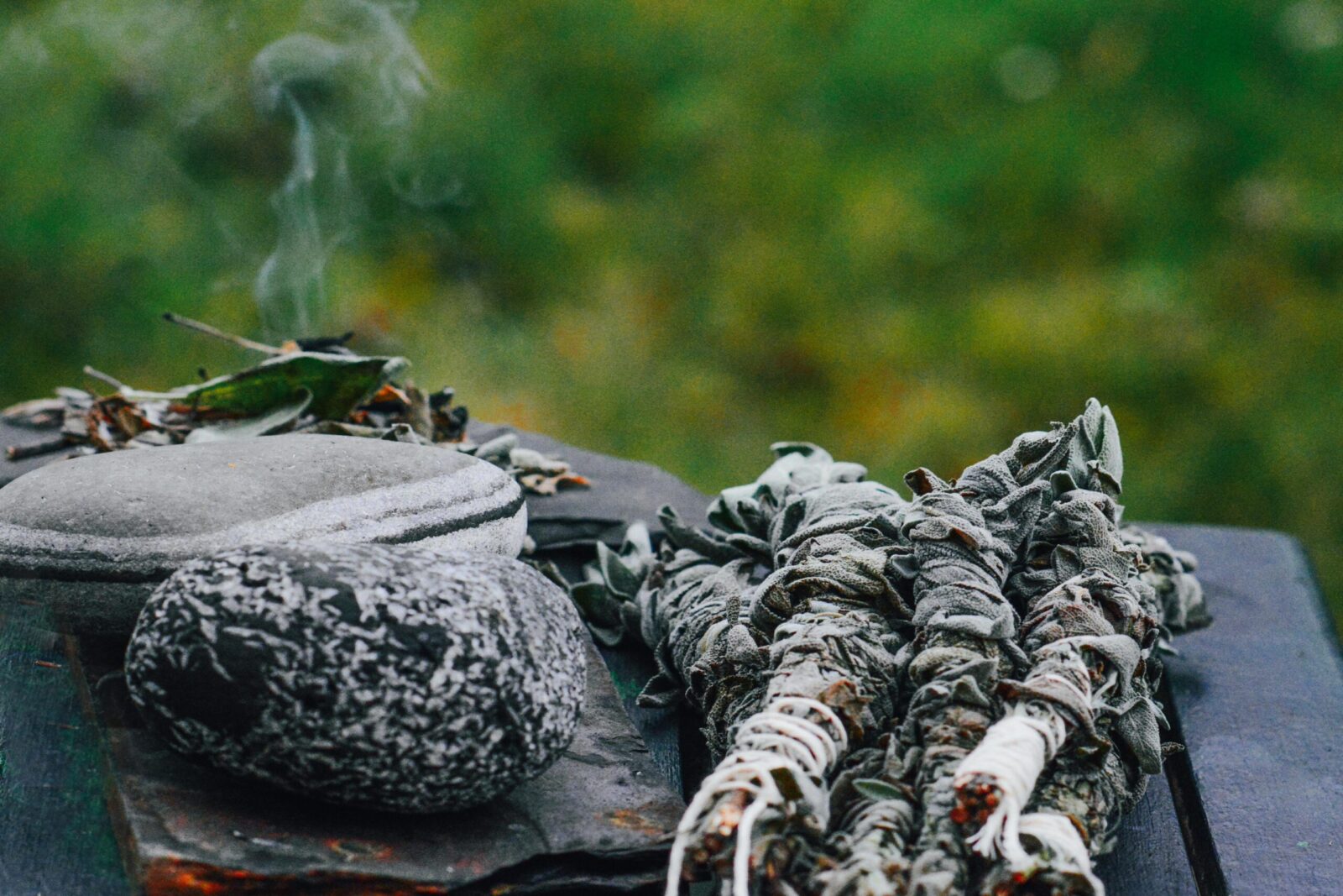 Herbal sage smudge and steaming hot stones on a wooden table in a natural outdoor setting.