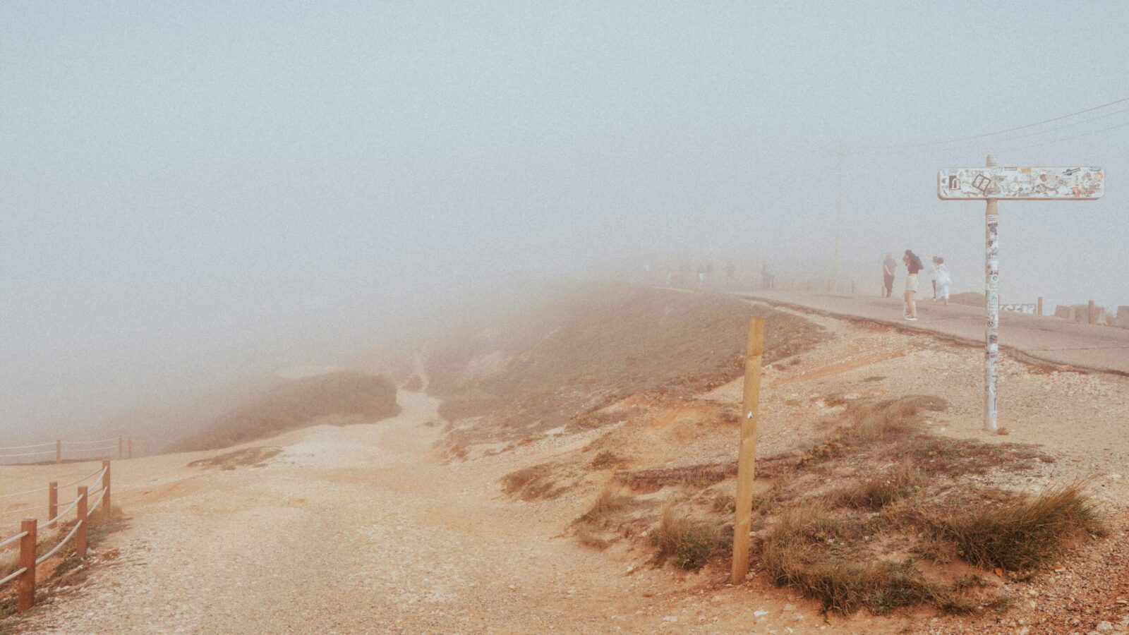 A misty coastal path in Nazaré, Portugal, with people walking along the foggy cliffs.