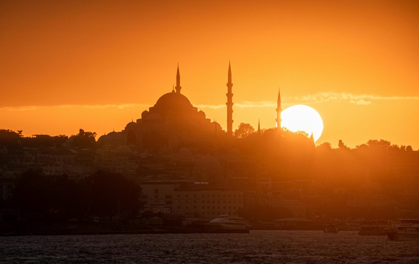 The iconic Istanbul skyline with a mosque silhouetted against a vibrant sunset over the Bosphorus Strait.