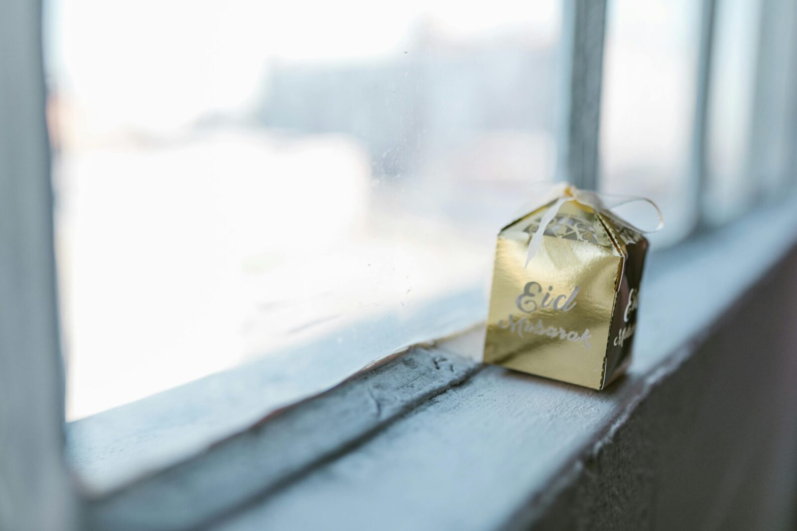 A golden Eid Mubarak gift box on a window sill, symbolizing celebration and tradition.