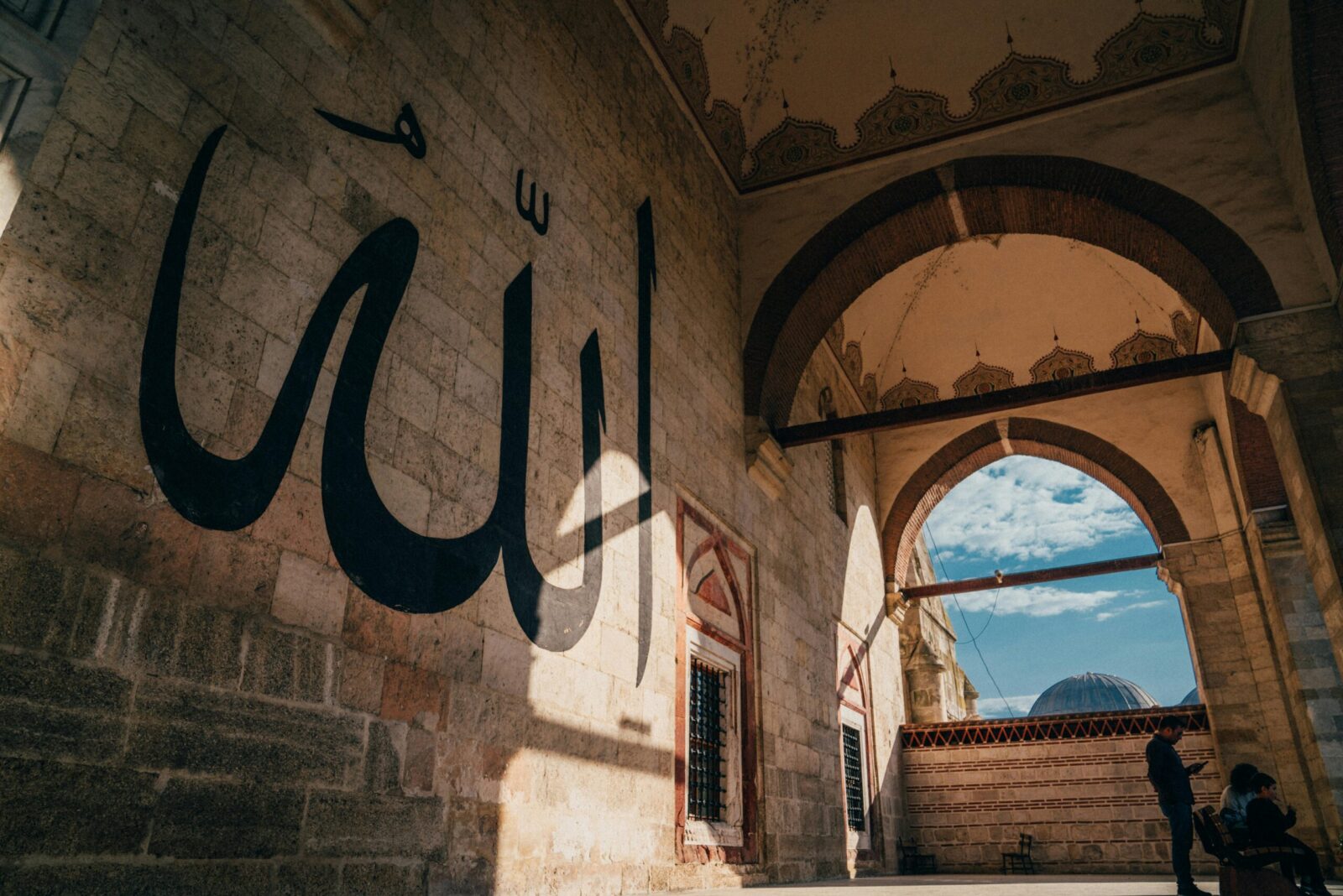 A beautiful view of a mosque interior showcasing Islamic calligraphy and architecture under a blue sky.