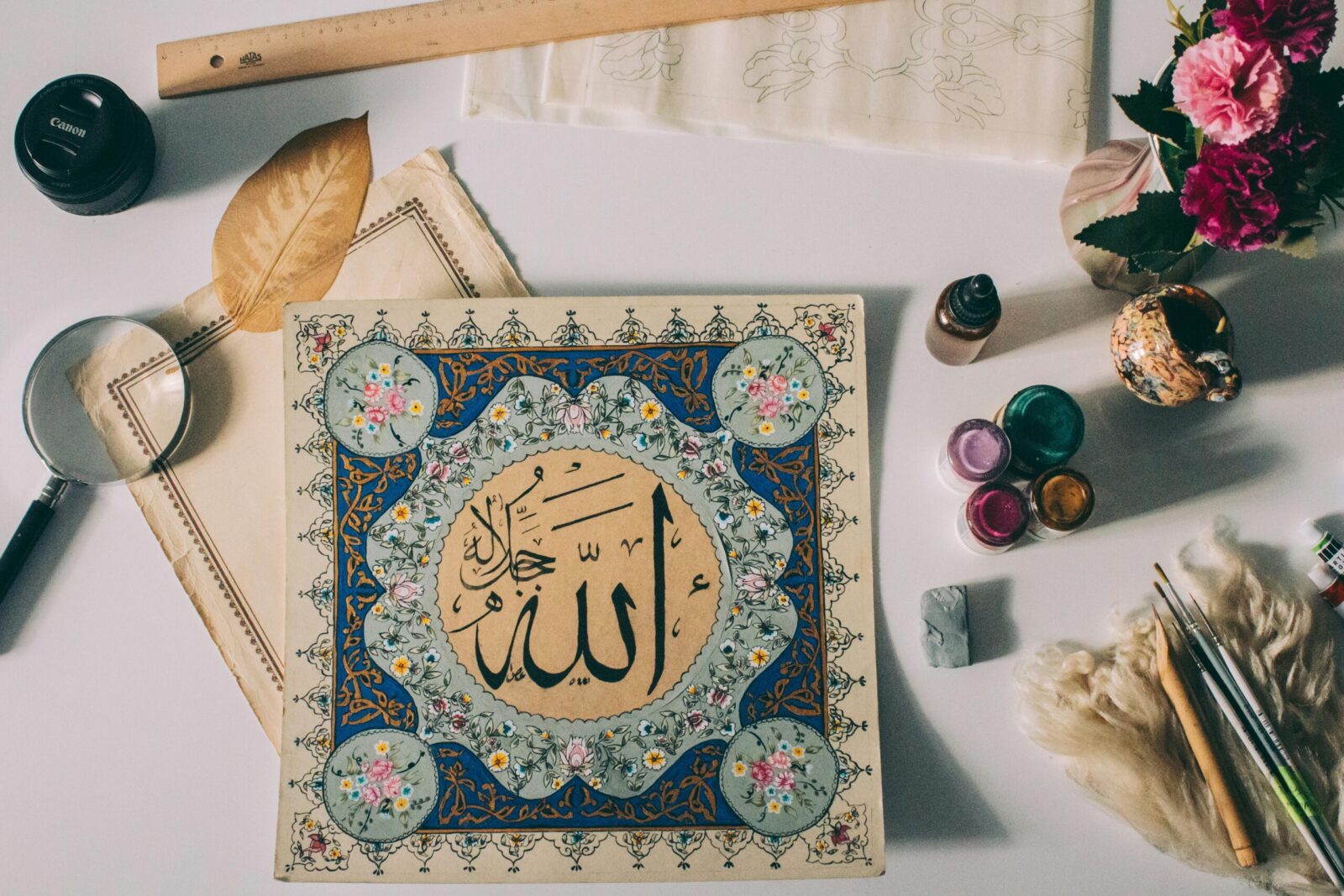 A beautiful flat lay of Islamic calligraphy artwork with paint supplies and decorative elements.