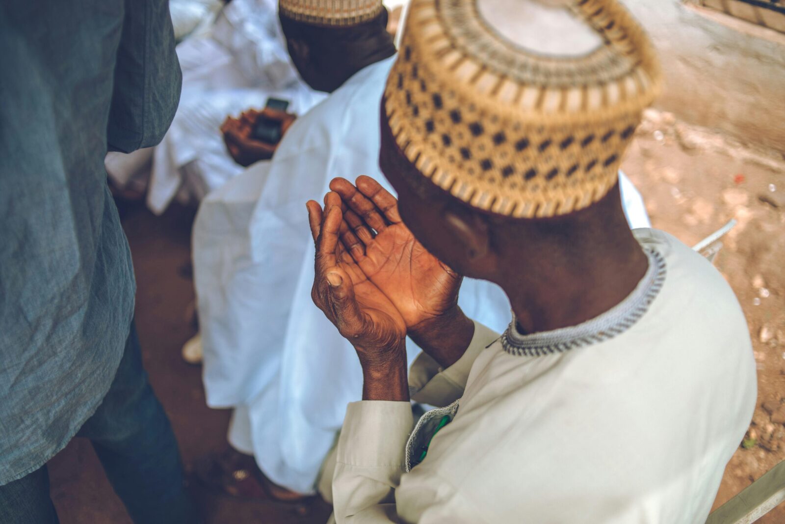 An elderly man in traditional attire praying outdoors in Okene, Nigeria.