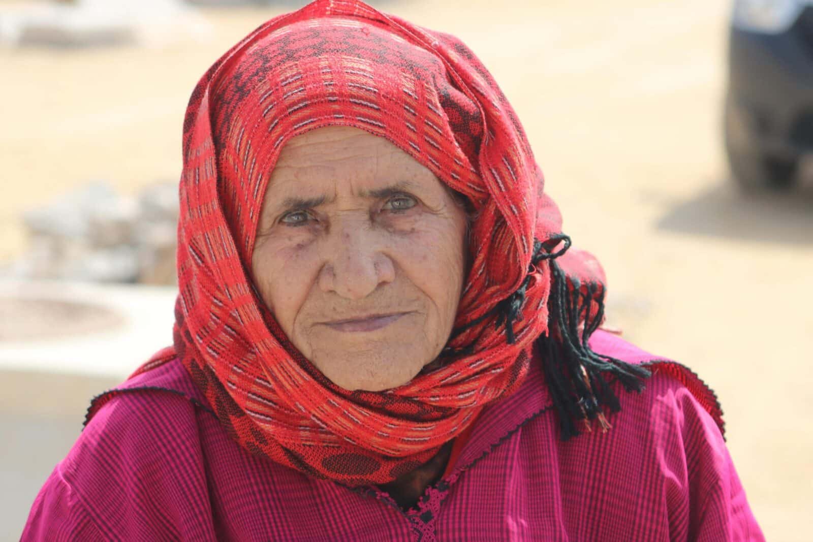 Portrait of an elderly Berber woman in traditional Moroccan attire, outdoors in bright daylight.