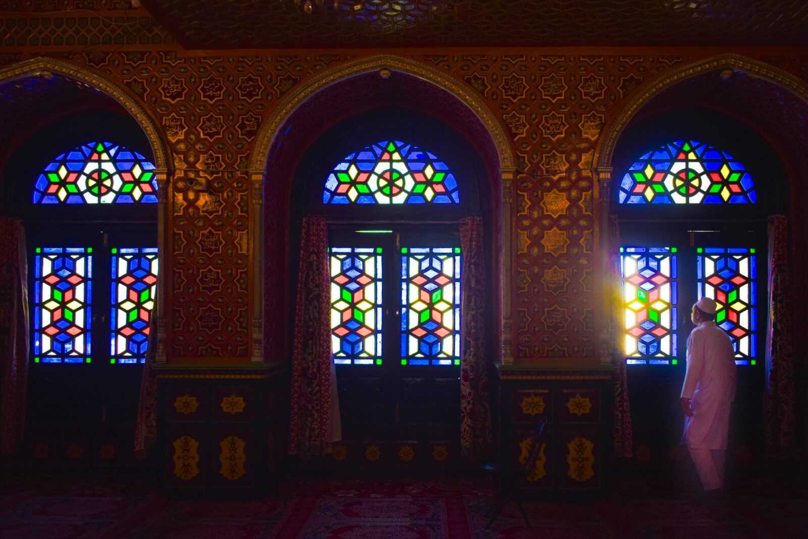 Vibrant stained glass windows inside a mosque in Srinagar with a person admiring the light.