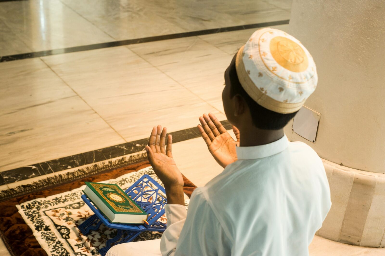 A young Muslim man praying indoors with the Quran in front of him, embodying devotion and peace.