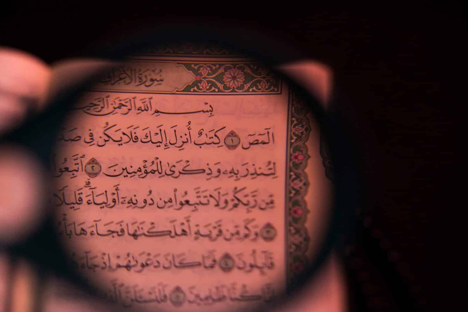 Detailed view of Quranic text seen through a magnifying glass, highlighting Arabic calligraphy and Islamic themes.