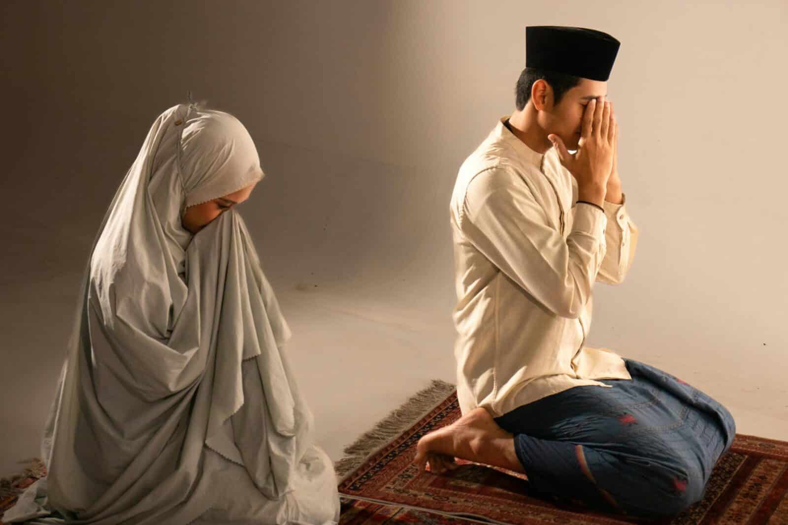 A Muslim couple in traditional attire praying indoors, reflecting devotion and culture.