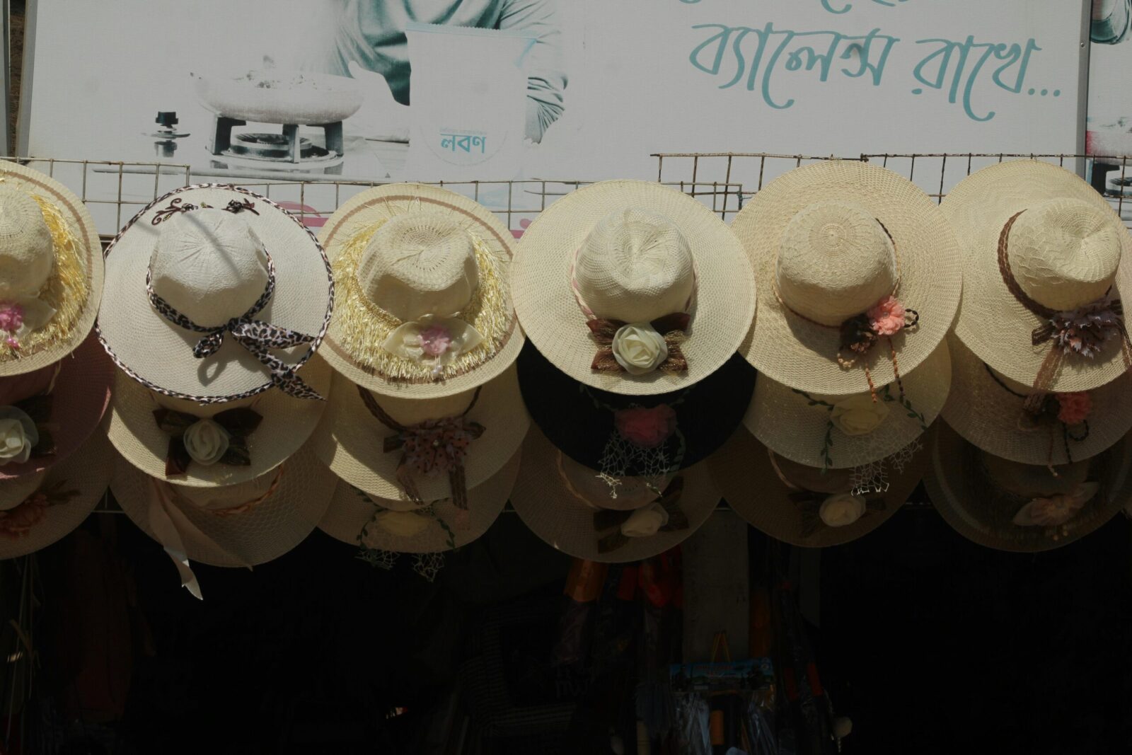 An array of straw hats with floral decorations, hanging in an outdoor market display.