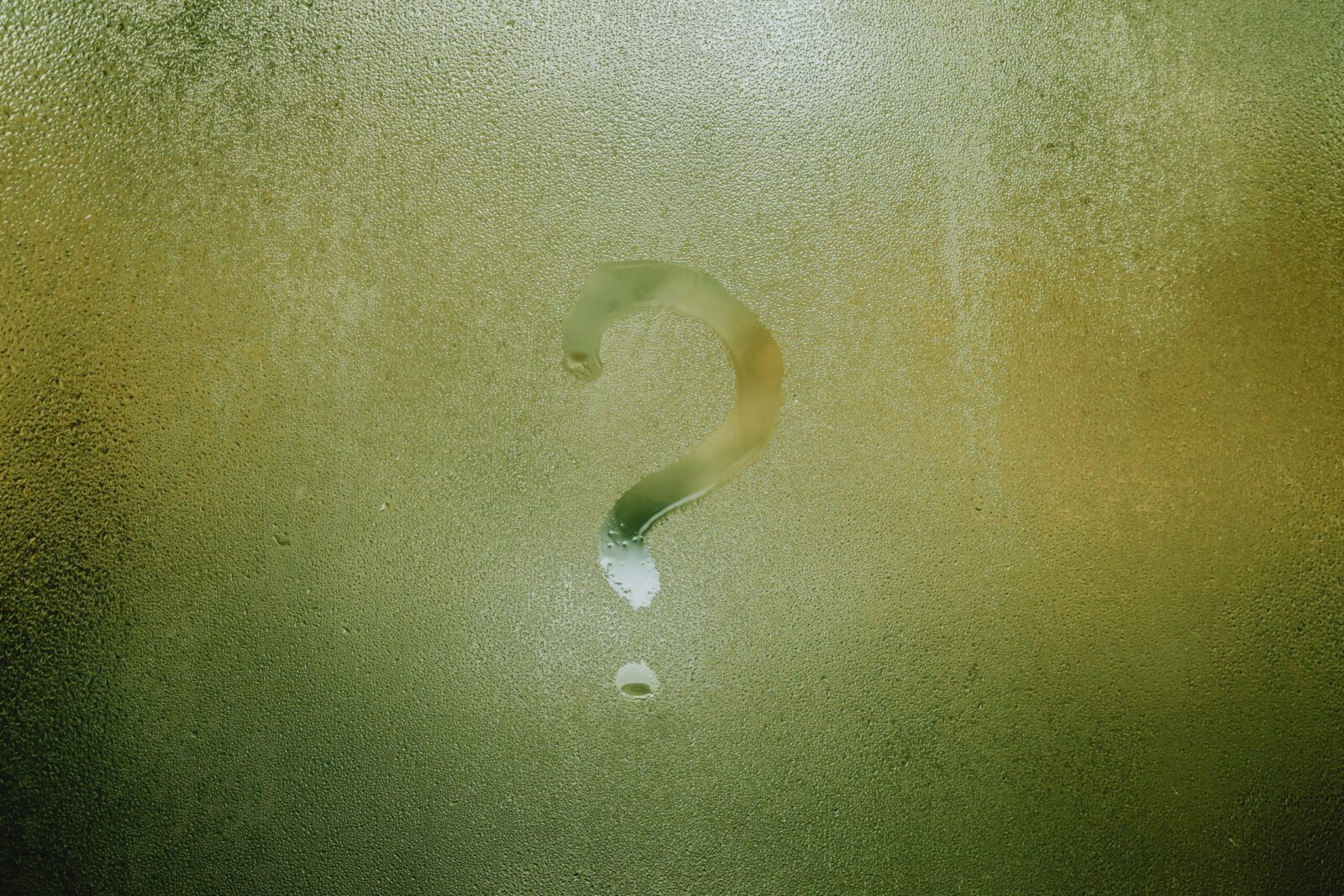 Translucent wet glass window covered with water drops with question mark on surface