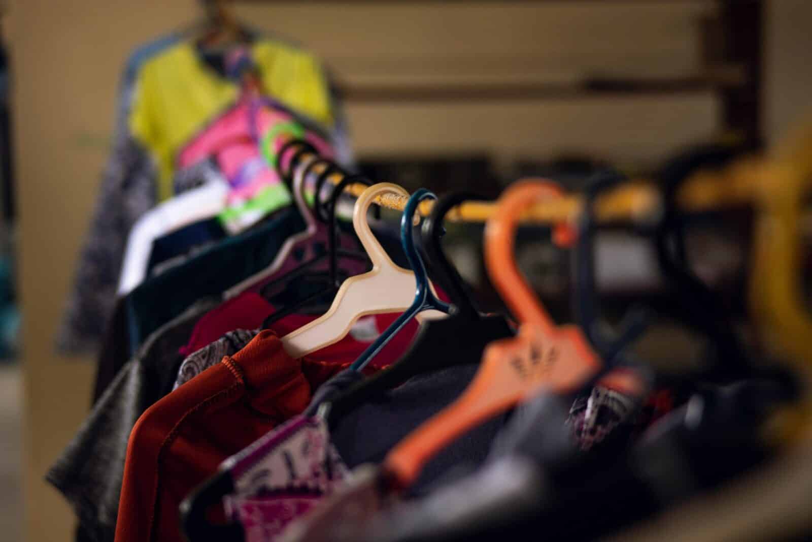 Stack of colorful trendy garments hanging on plastic hangers on long metal rack in modern light store on blurred background