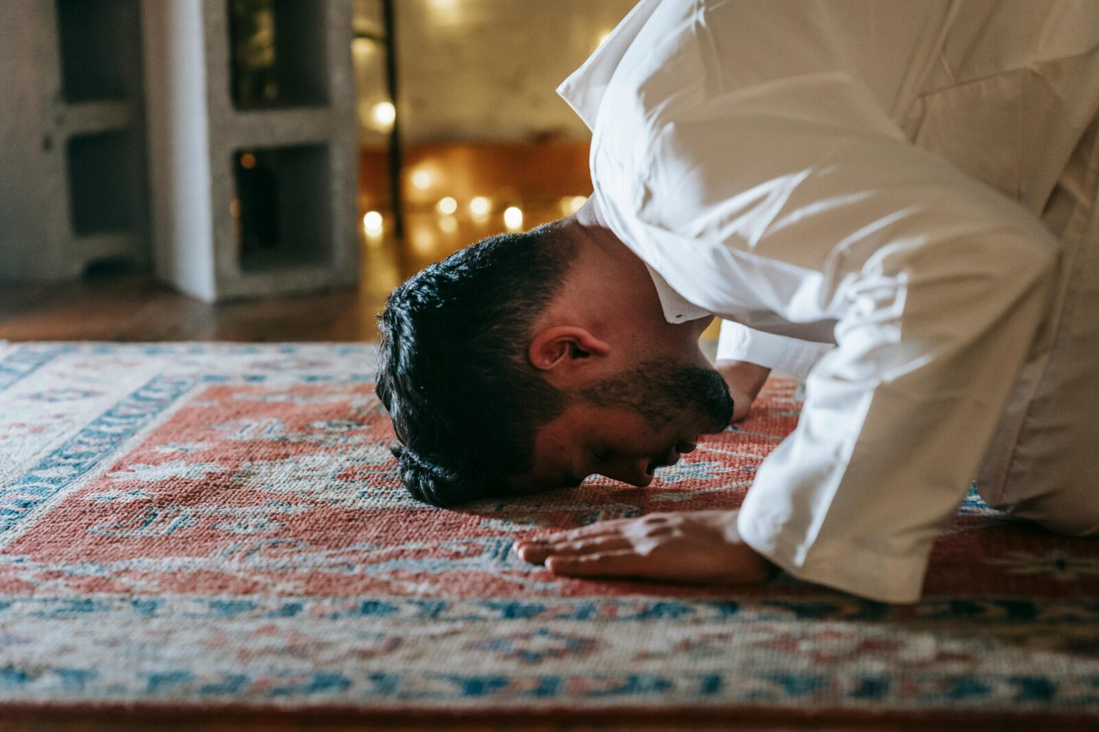 A Muslim man in traditional attire praying indoors, showcasing devotion and cultural faith.