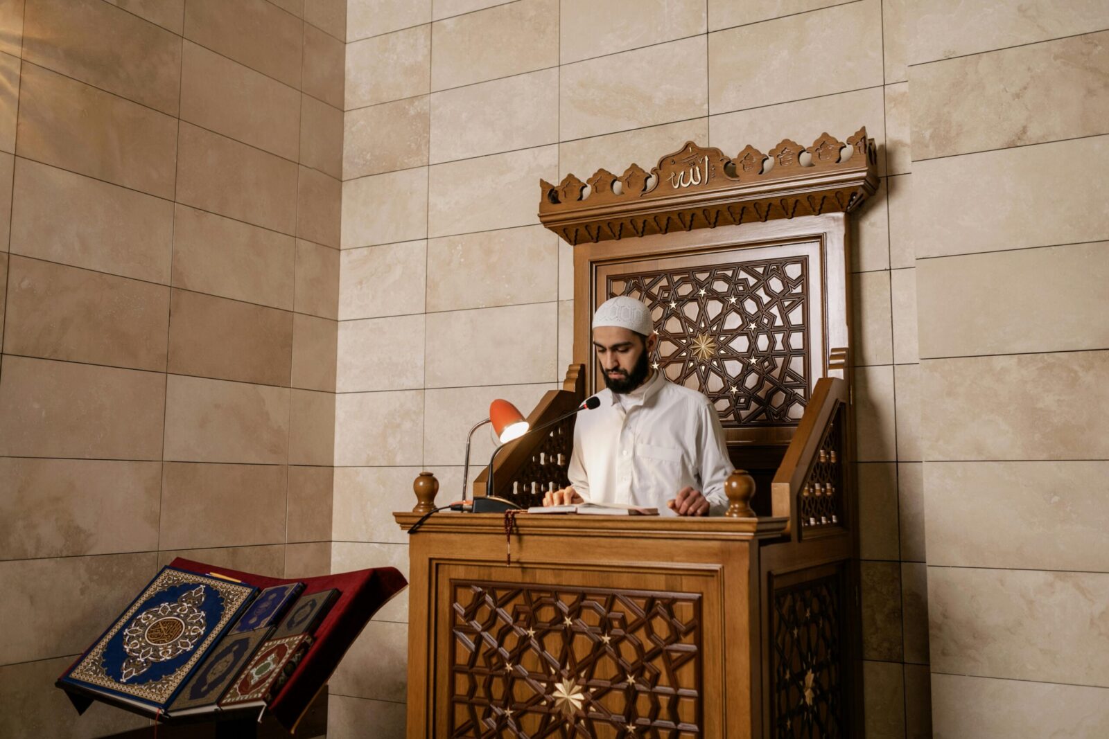 A Muslim man reading the Quran on a decorated mosque pulpit, symbolizing faith and tradition.
