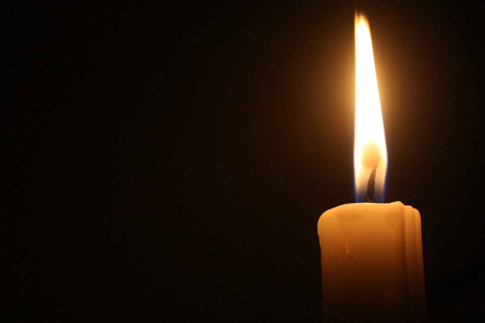 A close-up of a single lit candle with a bright flame against a dark backdrop.